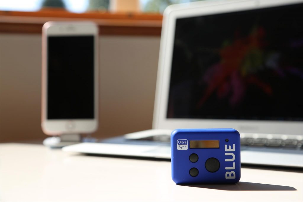 Image of UltraSync BLUE timecode over Bluetooth sync solution, with an iphone and computer highlighting the simplicity of capturing footage to editing.